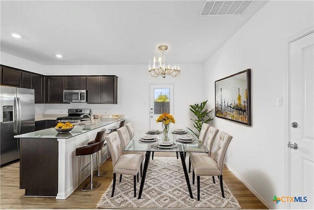 kitchen with dark brown cabinetry, hanging light fixtures, light hardwood / wood-style flooring, a chandelier, and appliances with stainless steel finishes