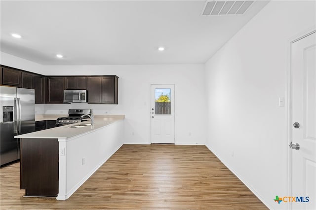 kitchen with kitchen peninsula, appliances with stainless steel finishes, dark brown cabinetry, sink, and light hardwood / wood-style floors