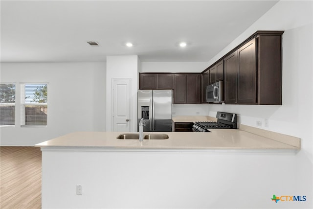 kitchen with sink, dark brown cabinetry, light hardwood / wood-style floors, kitchen peninsula, and stainless steel appliances