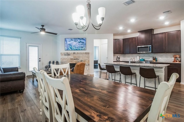 dining room with dark hardwood / wood-style floors, ceiling fan with notable chandelier, and a fireplace