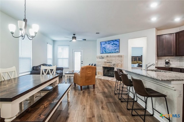 dining room with hardwood / wood-style flooring, a stone fireplace, ceiling fan with notable chandelier, and sink