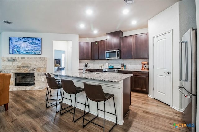 kitchen with a breakfast bar, appliances with stainless steel finishes, a kitchen island with sink, hardwood / wood-style floors, and a stone fireplace