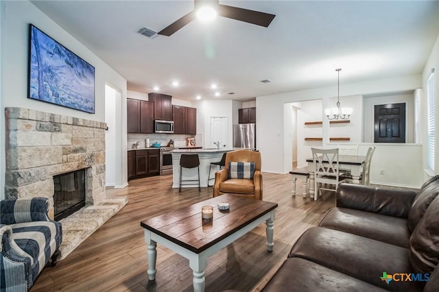 living room with dark hardwood / wood-style flooring, sink, ceiling fan with notable chandelier, and a fireplace