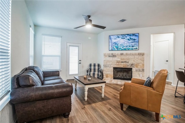 living room featuring hardwood / wood-style floors, a stone fireplace, and ceiling fan