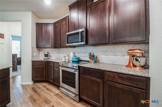 kitchen with light stone counters, tasteful backsplash, dark brown cabinets, light wood-type flooring, and stainless steel appliances