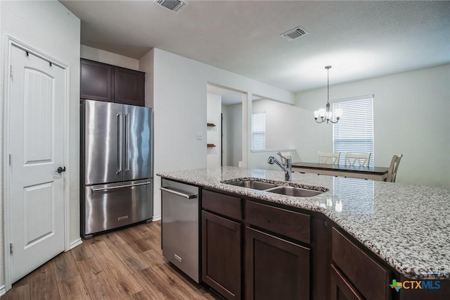 kitchen with dark wood-type flooring, sink, dark brown cabinets, stainless steel appliances, and a kitchen island with sink