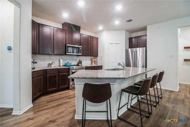 kitchen with appliances with stainless steel finishes, an island with sink, sink, a kitchen bar, and hardwood / wood-style flooring