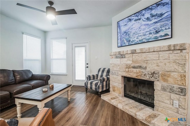 living room featuring wood-type flooring, a stone fireplace, and ceiling fan