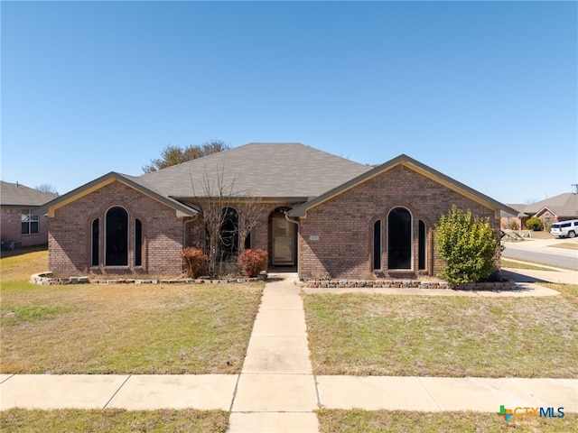 view of front of house with roof with shingles, a front yard, and brick siding