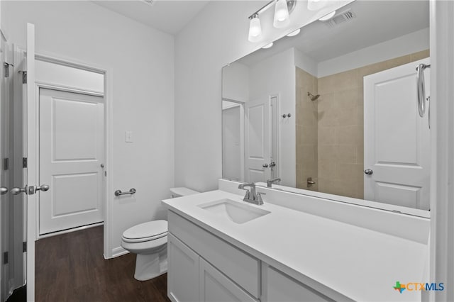 bathroom with toilet, hardwood / wood-style floors, vanity, and a tile shower