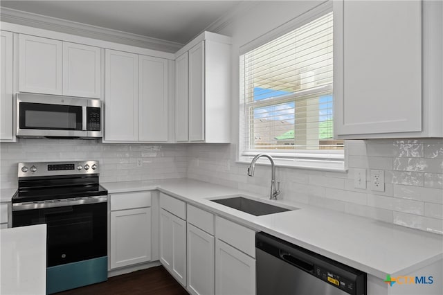 kitchen with sink, decorative backsplash, ornamental molding, appliances with stainless steel finishes, and white cabinetry