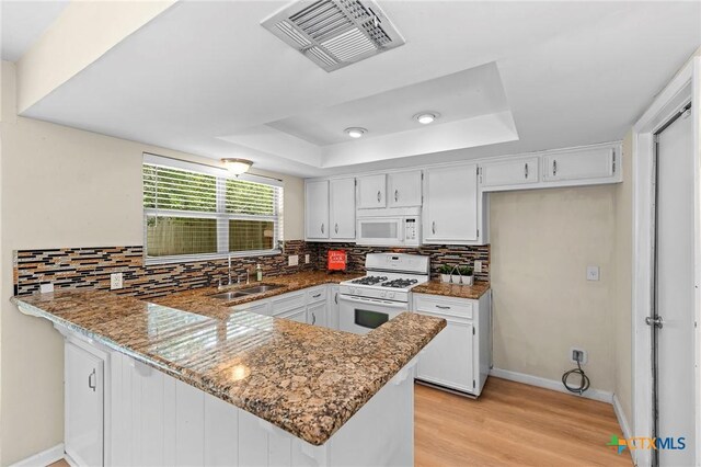 907 Great Oaks Cv, Round Rock, TX 78681 - kitchen with white appliances, a peninsula, a tray ceiling, decorative backsplash, and light wood-style flooring
