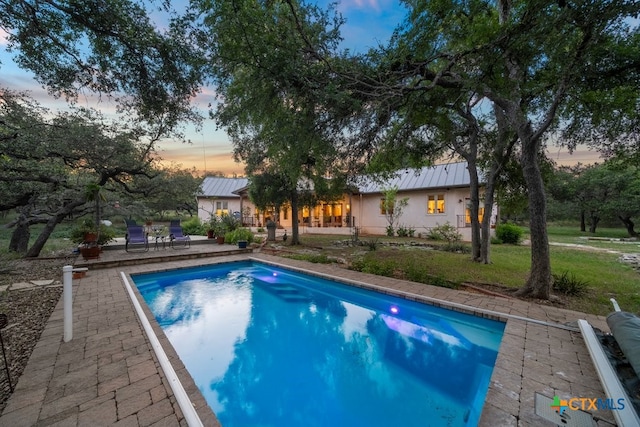 pool at dusk with a lawn and a patio area