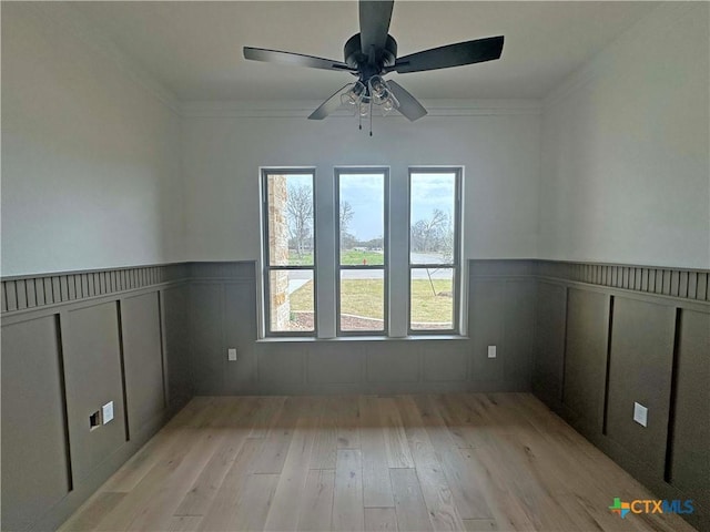 empty room with ornamental molding, wood finished floors, and wainscoting