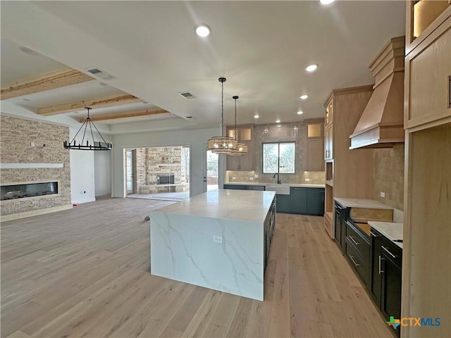 kitchen featuring light stone counters, a fireplace, custom range hood, visible vents, and light wood-style flooring