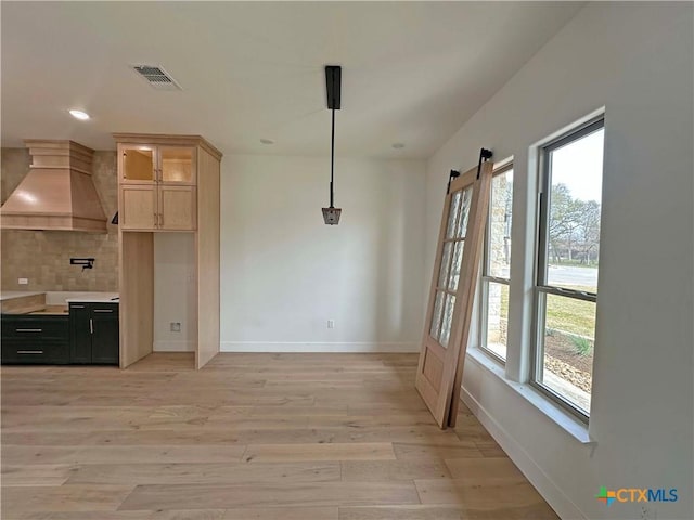 kitchen featuring light wood-style flooring, visible vents, baseboards, custom exhaust hood, and tasteful backsplash