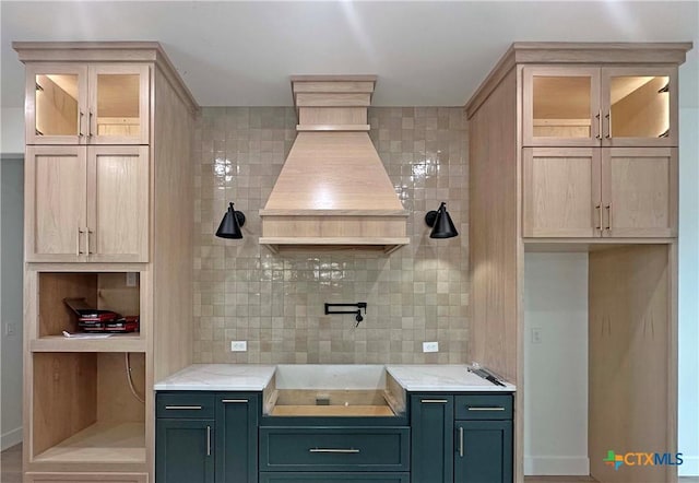 kitchen with custom range hood, glass insert cabinets, decorative backsplash, and light stone counters