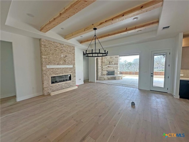 unfurnished living room featuring a fireplace, visible vents, an inviting chandelier, light wood-style floors, and beamed ceiling