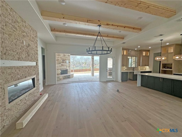 unfurnished living room with beam ceiling, light wood finished floors, visible vents, an inviting chandelier, and a stone fireplace