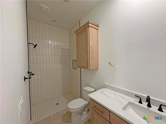 full bath featuring toilet, a tile shower, and vanity