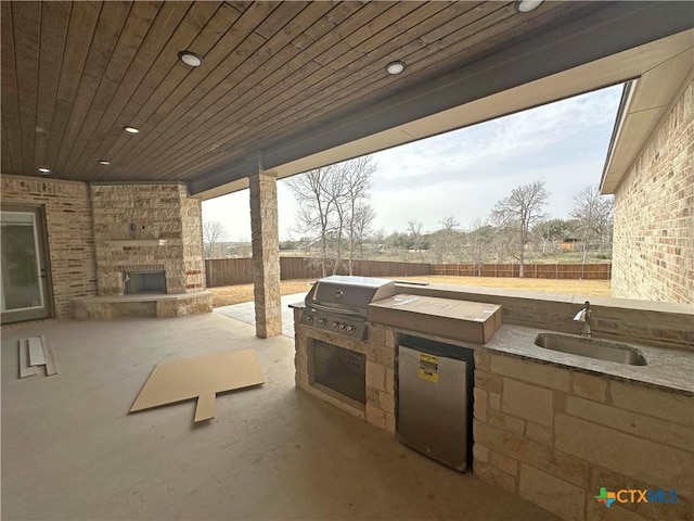 view of patio featuring a fenced backyard, an outdoor stone fireplace, a sink, a grill, and exterior kitchen