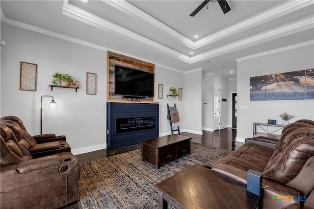 living room featuring ornamental molding, a raised ceiling, ceiling fan, dark wood-type flooring, and a fireplace