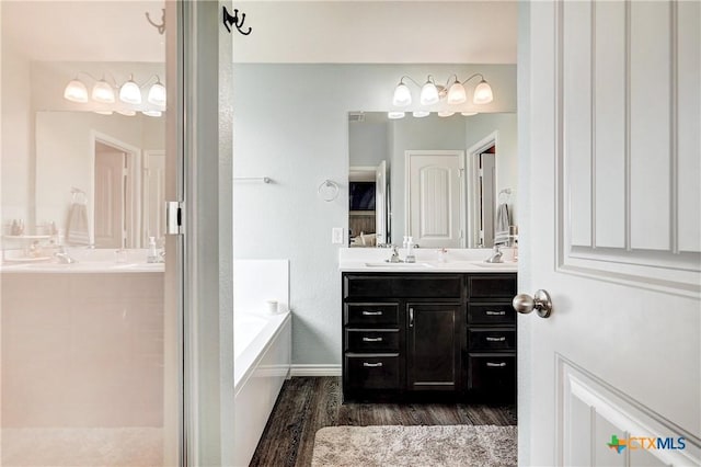 full bath with vanity, a garden tub, and wood finished floors