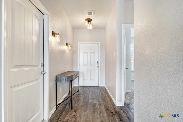 hallway with visible vents, dark wood-type flooring, baseboards, and a textured wall