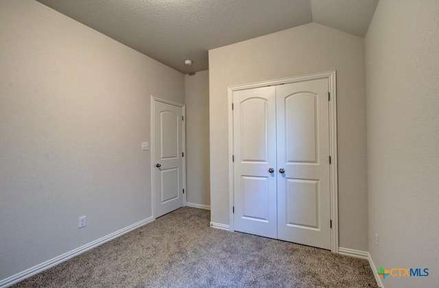 unfurnished bedroom featuring light carpet, a textured ceiling, vaulted ceiling, and a closet