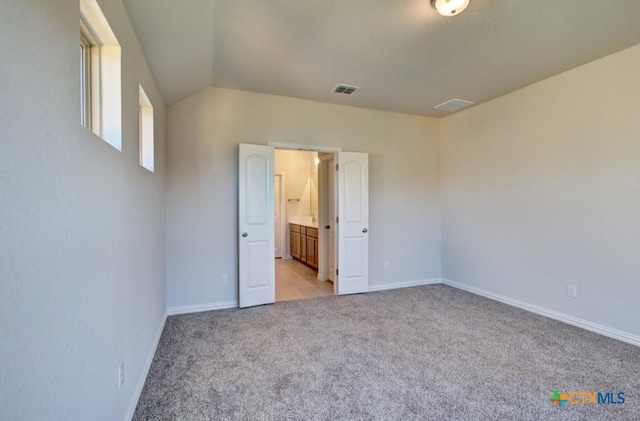 unfurnished bedroom with light colored carpet, connected bathroom, and vaulted ceiling