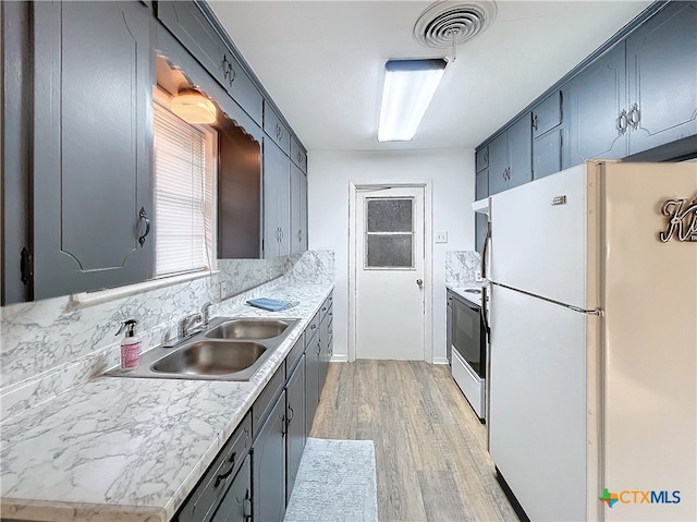 kitchen featuring stainless steel electric range, white refrigerator, sink, light wood-type flooring, and light stone counters