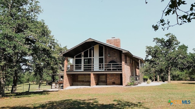 rear view of house with a patio area, brick siding, a balcony, a yard, and a chimney