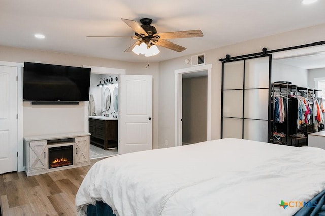 bedroom with a warm lit fireplace, recessed lighting, a barn door, visible vents, and light wood-style floors