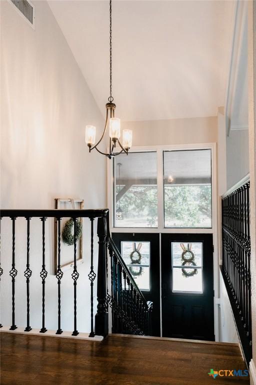 foyer entrance with a chandelier, high vaulted ceiling, visible vents, and wood finished floors