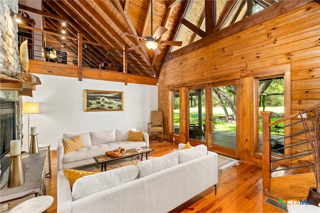 living room featuring light hardwood / wood-style floors, high vaulted ceiling, ceiling fan, beam ceiling, and a fireplace