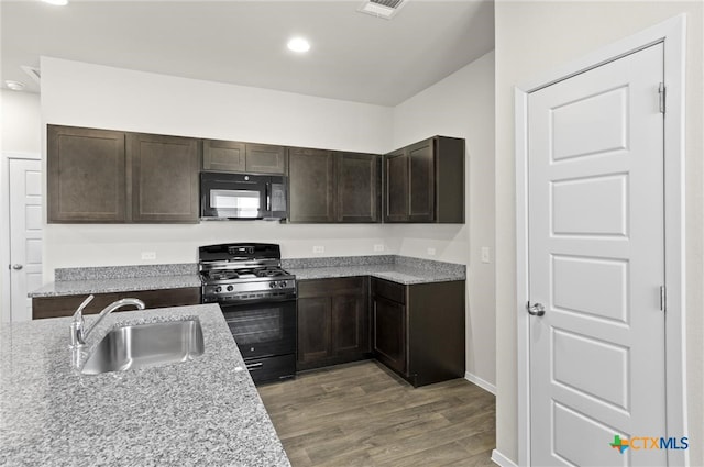 kitchen featuring dark brown cabinetry, sink, light stone counters, light hardwood / wood-style floors, and black appliances