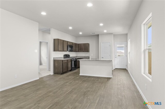 kitchen featuring wood-type flooring, a kitchen island with sink, a healthy amount of sunlight, and black appliances