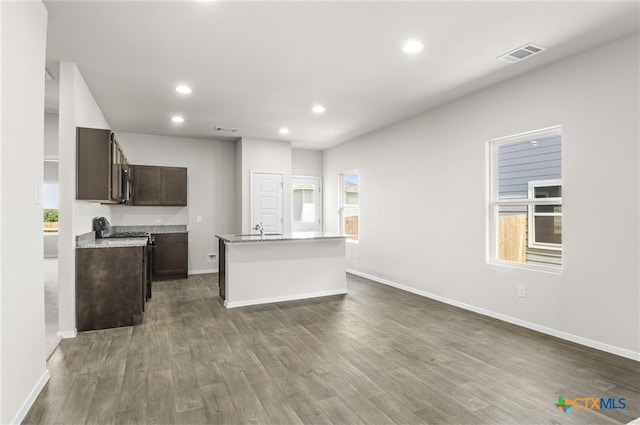 kitchen with dark brown cabinetry, dark wood-type flooring, sink, electric range, and a center island with sink