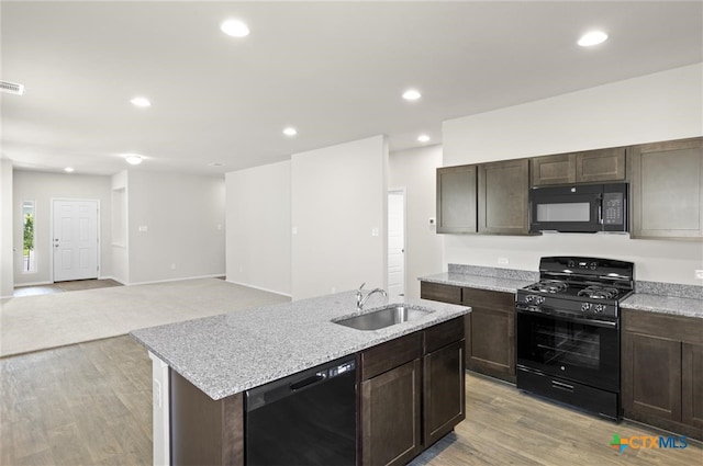 kitchen with dark brown cabinetry, sink, an island with sink, light hardwood / wood-style floors, and black appliances