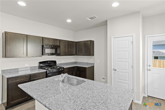 kitchen featuring dark brown cabinetry, sink, light stone counters, light hardwood / wood-style floors, and black appliances