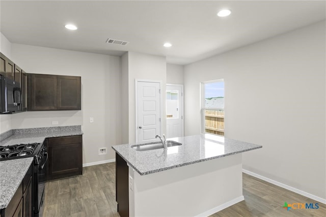 kitchen featuring light stone countertops, sink, dark hardwood / wood-style flooring, an island with sink, and black appliances