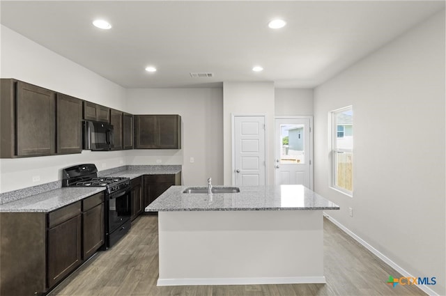 kitchen with a kitchen island with sink, black appliances, light stone countertops, light wood-type flooring, and dark brown cabinets