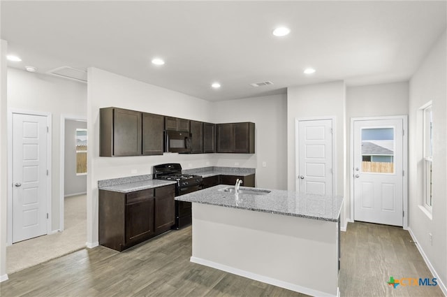 kitchen featuring sink, light stone counters, light hardwood / wood-style flooring, a kitchen island with sink, and black appliances