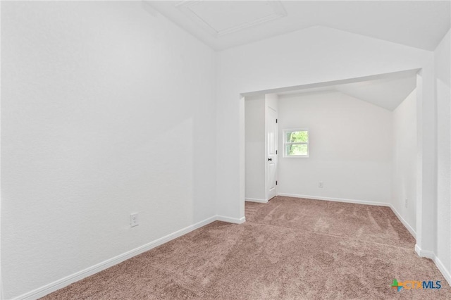 empty room with attic access, lofted ceiling, carpet flooring, and baseboards