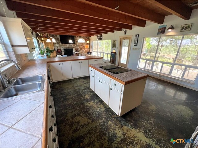 184 Guadalupe Hills Ln, Seguin, TX 78155 - kitchen with tile countertops, black electric cooktop, white cabinets, beamed ceiling, and a fireplace