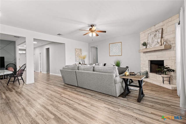 living room with a stone fireplace, ceiling fan, and wood-type flooring