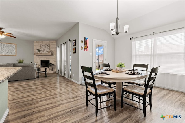 dining area featuring a stone fireplace, a healthy amount of sunlight, ceiling fan with notable chandelier, and hardwood / wood-style flooring