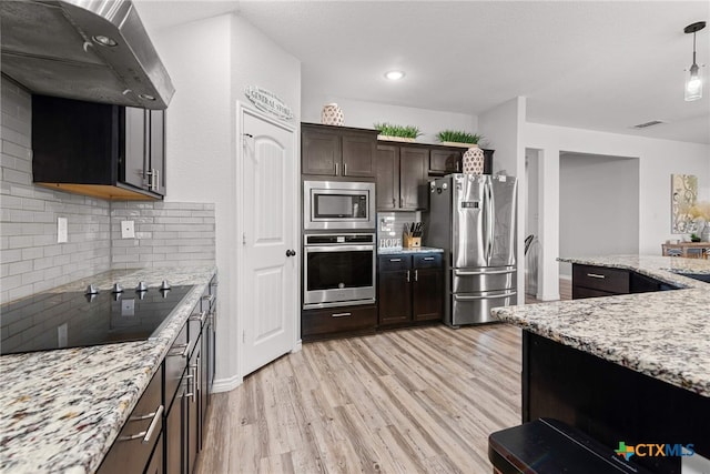 kitchen with decorative backsplash, light stone counters, stainless steel appliances, exhaust hood, and light hardwood / wood-style floors