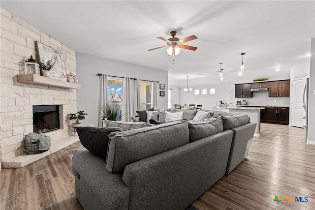 living room with a fireplace, wood-type flooring, and ceiling fan with notable chandelier