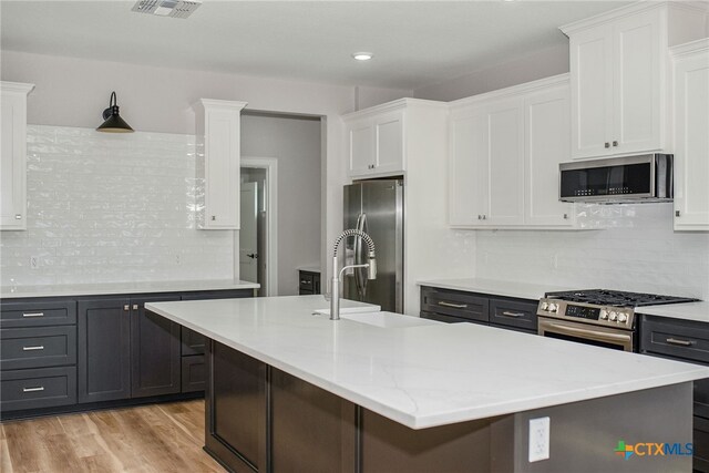 kitchen with an island with sink, white cabinets, backsplash, and appliances with stainless steel finishes